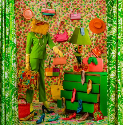 Highly patterned image of a standing figure with a purse over their head. They are holding several bags, and are surrounded by shoes. There are hats and bags on the wall behind them. A green dresser to the left had high heels coming out of the drawers.